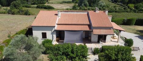 A two-story house with a tiled roof, a covered porch, and a garden with various plants and trees.