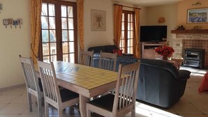 Een woonkamer met een eettafel, stoelen, een bank, een open haard en een televisie.