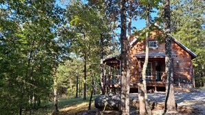 Un chalet rustique entouré de grands arbres, au cœur d’une forêt.