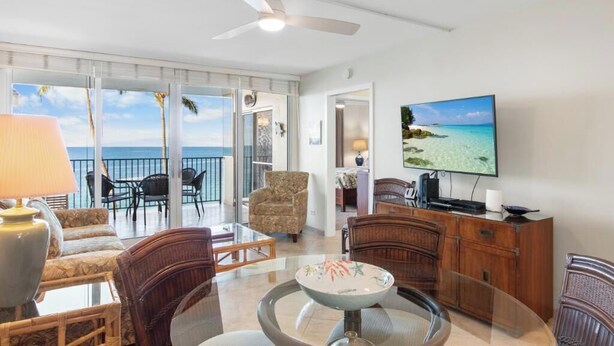 A living room with a glass table, chairs, a television, and a view of the ocean.