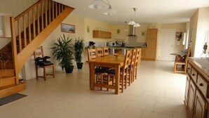Amplia sala de estar con una escalera de madera, una mesa de comedor con sillas, una zona de cocina y una planta grande en maceta.