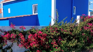 Un edificio azul con tejado de tejas rojas, una ventana blanca y una pequeña antena en el tejado.