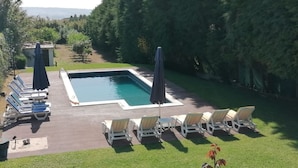 Una piscina rectangular con cubierta de madera, rodeada de sillas de descanso y sombrillas.
