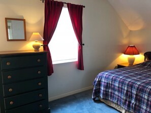 A bedroom with a bed, a dresser, a nightstand, a lamp, and a window with red curtains. - Fly-in place to stay close to The Villages (Fruitland Park)