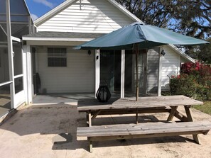A wooden picnic table with an umbrella, a grill, and a house with a covered porch. - Fly-in place to stay close to The Villages (Fruitland Park)