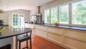 A kitchen with a large island, white cabinets, a stainless steel range hood, and a window with a view of greenery. - Valbonne Quiet villa with magnesium pool (Valbonne)