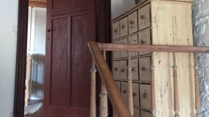 Una escalera de madera conduce a un cuarto con pared de ladrillo blanco y un mueble de madera con varios cajones.