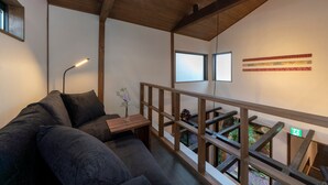 A modern living room with a wooden ceiling, a sofa, a small table with a vase, and a balcony with a railing. - Hinaya Higashiyama (Kanazawa)