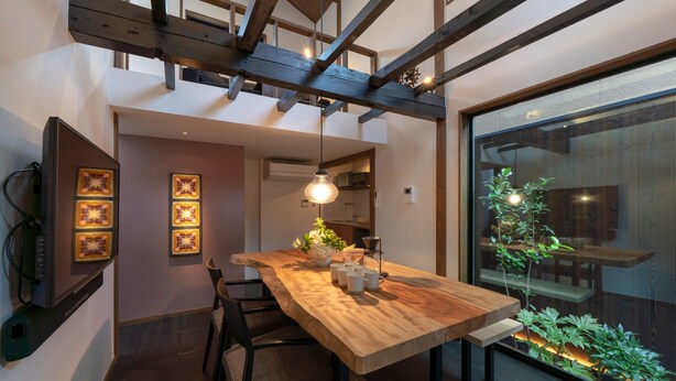 A modern dining area with a wooden table, chairs, and pendant lighting. A staircase is visible in the background, leading to an upper level. - Hinaya Higashiyama (Kanazawa)