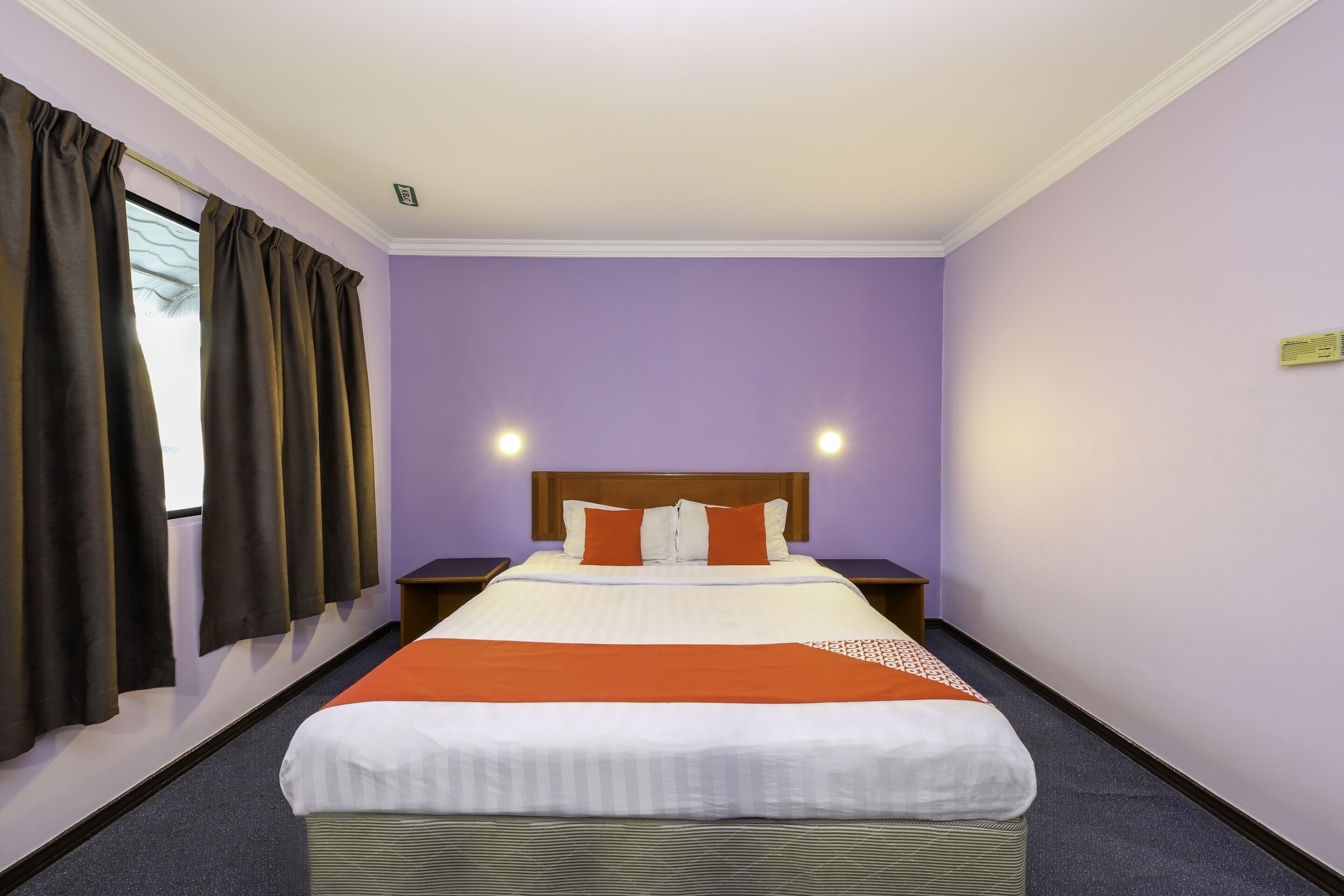 Una habitación de hotel con una cama grande, dos mesitas de noche y una ventana con cortinas.