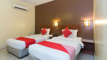 A hotel room with two beds, each with a red and white bedspread, a bedside table with a phone, and wall-mounted lights.