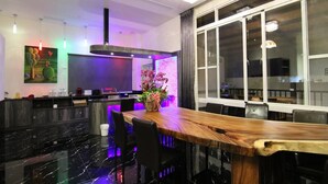 Un área de bar moderna con mostrador de madera, piso de mármol negro y un amplio ventanal con cortinas.