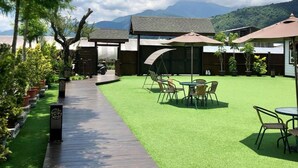 Un patio con césped artificial, mobiliario exterior y una terraza de madera que conduce a un edificio.
