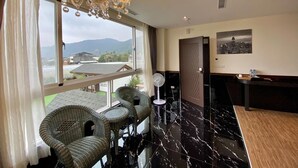 Habitación de hotel con un ventanal grande, sillas de mimbre, un candelabro, suelo de mármol, una mesa de recepción y vistas a la ciudad.