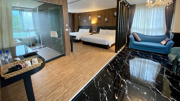 Habitación de hotel con ducha envuelta en vidrio, cama con ropa de cama blanca, sofá azul y suelo de mármol.