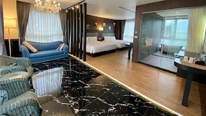 Una habitación de hotel moderna con una cama grande, un sofá independiente, una zona de ducha con mampara de vidrio y suelo de mármol.