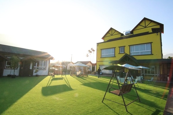 A yellow building with a large patio area, including a swing set and umbrellas. - Puli Diary (Puli)