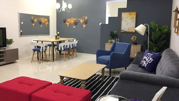 A modern living room with a grey sofa, red ottomans, a blue armchair, and a dining area with a round table and chairs. - Sandakan Hill Terrace 3 (Sandakan)