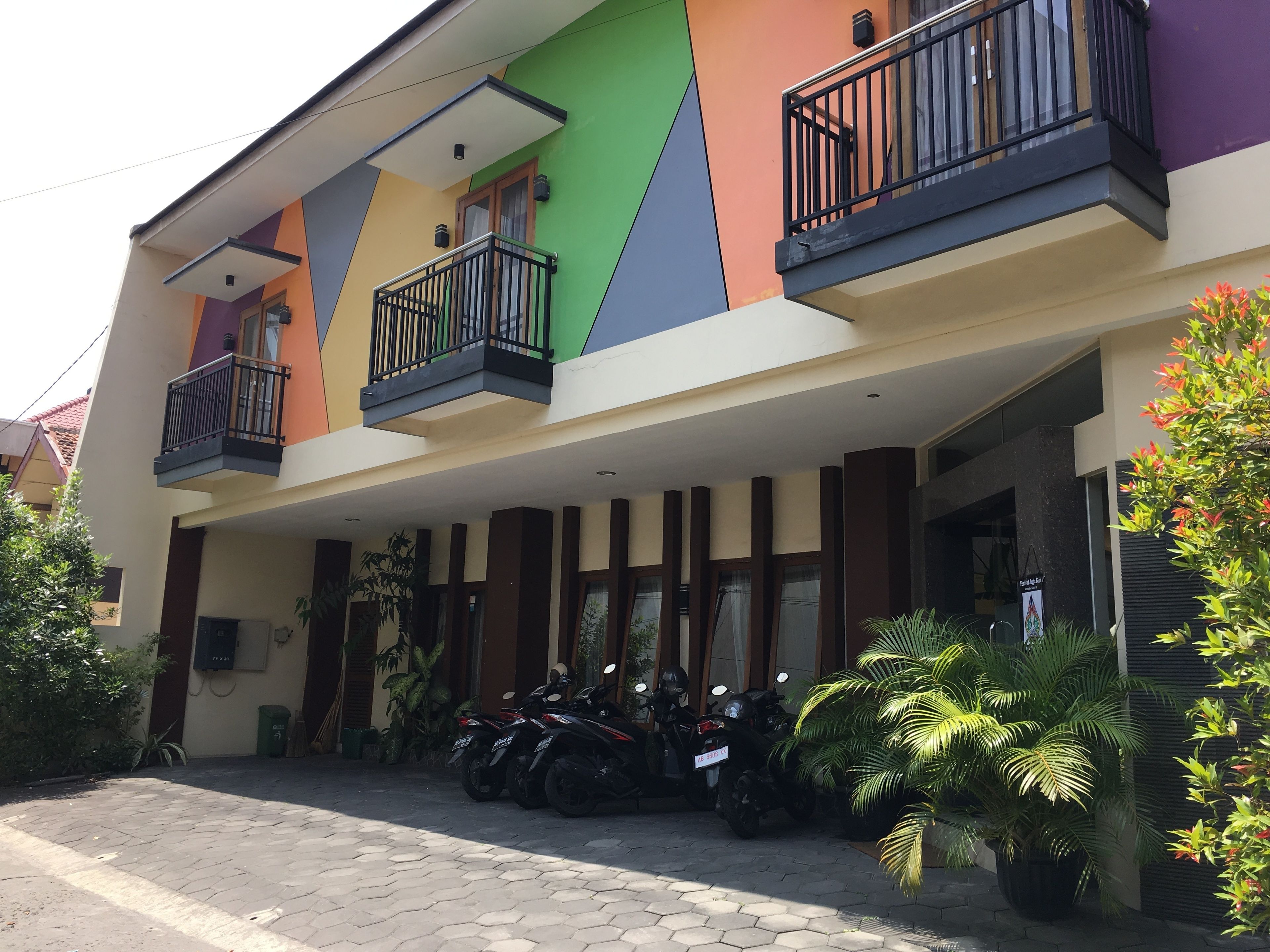 A multi-story building with balconies, a covered entrance, and parked motorcycles.