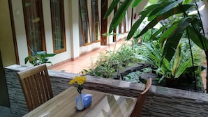 Ein Holztisch mit einer Vase voller gelber Blumen, vor einer Gartenkulisse mit verschiedenen Pflanzen und einem kleinen Teich.