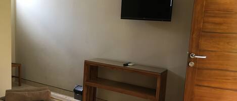 Un dormitorio con una cama, una mesita de noche de madera, un televisor montado en la pared y una puerta.