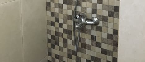 A shower with a checkered tile wall, a handheld showerhead, and a wall-mounted faucet.