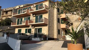 Un edificio residencial de varios pisos con balcones, un coche estacionado al frente y una planta en maceta en primer plano.