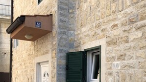 Un edificio de piedra con una puerta, una ventana con contraventanas verdes y un medidor de servicios.