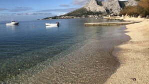 Una playa despejada con barcos, una montaña rocosa y un pequeño pueblo al fondo.