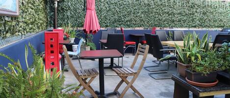 Un espace extérieur aménagé en terrasse, avec des tables et des chaises, des plantes en pot et une boîte aux lettres rouge.