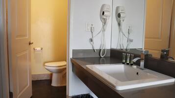 Une salle de bain avec un lavabo blanc, un miroir et deux sèche-cheveux fixés au mur.