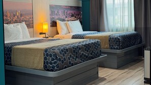 A hotel room with two beds, a cityscape mural on the wall, a window with curtains, and a nightstand with a lamp. - Hometel Suites - Los Angeles (Koreatown) (Los Angeles)