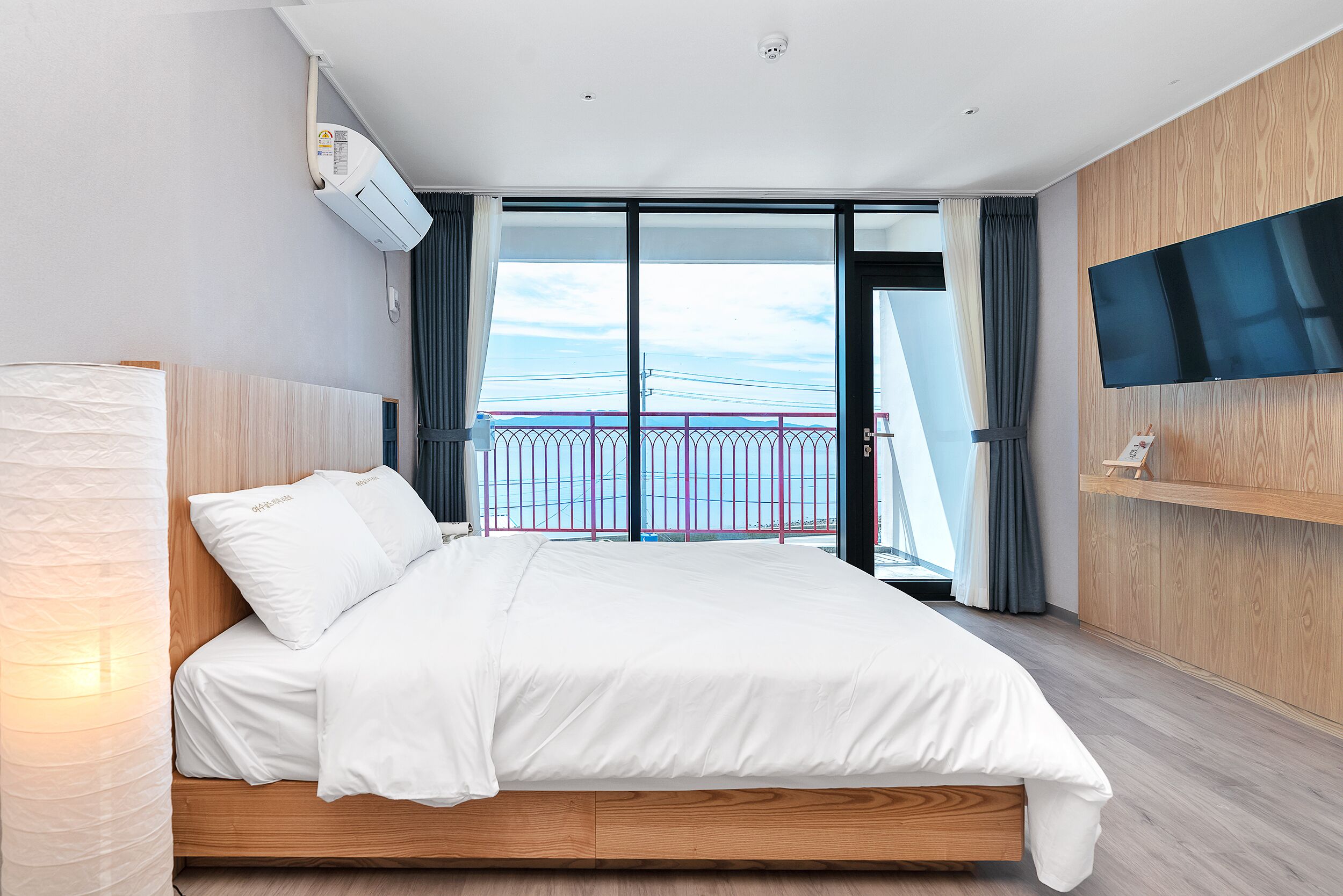 A modern hotel room with a large bed, a flat-screen TV mounted on the wall, and a balcony with a view of the city skyline.