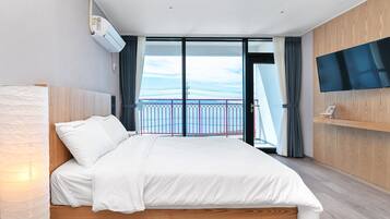 A modern hotel room with a large bed, a flat-screen TV mounted on the wall, and a balcony with a view of the city skyline.