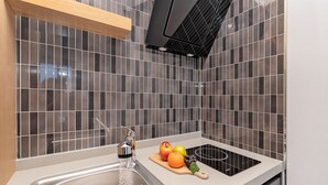 A kitchen with a stainless steel sink, a wooden cutting board with fruits, and a black range hood. - Gold Beach Resort (Yeosu)