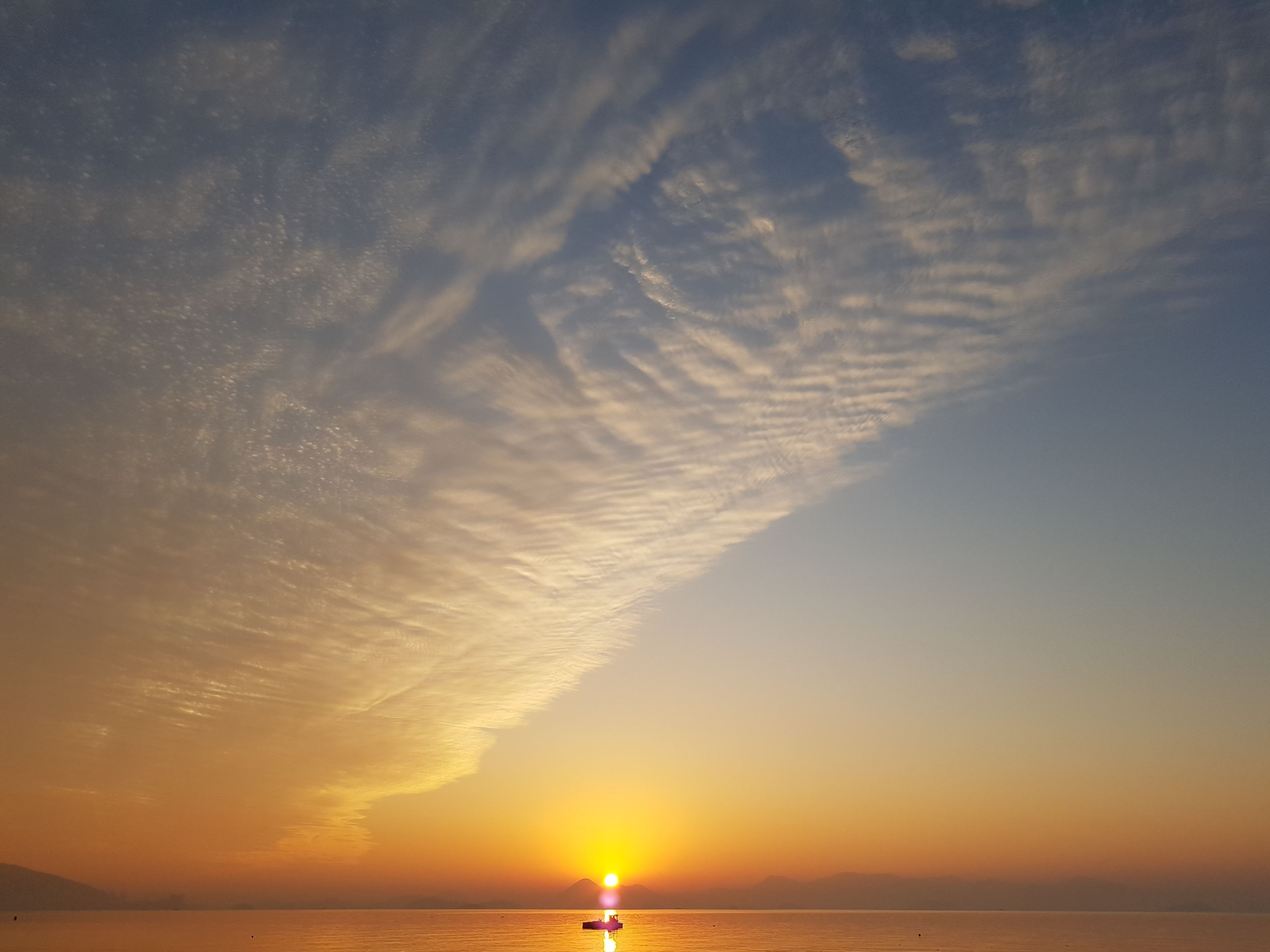 A sunset over a calm sea with a boat in the foreground and a mountain in the distance.