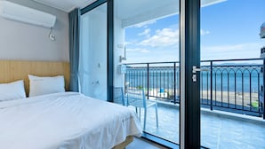 A hotel room with a bed, a balcony with a view of the sea, and a small table with chairs. - Gold Beach Resort (Yeosu)