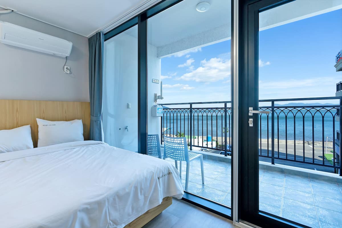 A hotel room with a bed, a balcony with a view of the sea, and a small table with chairs.