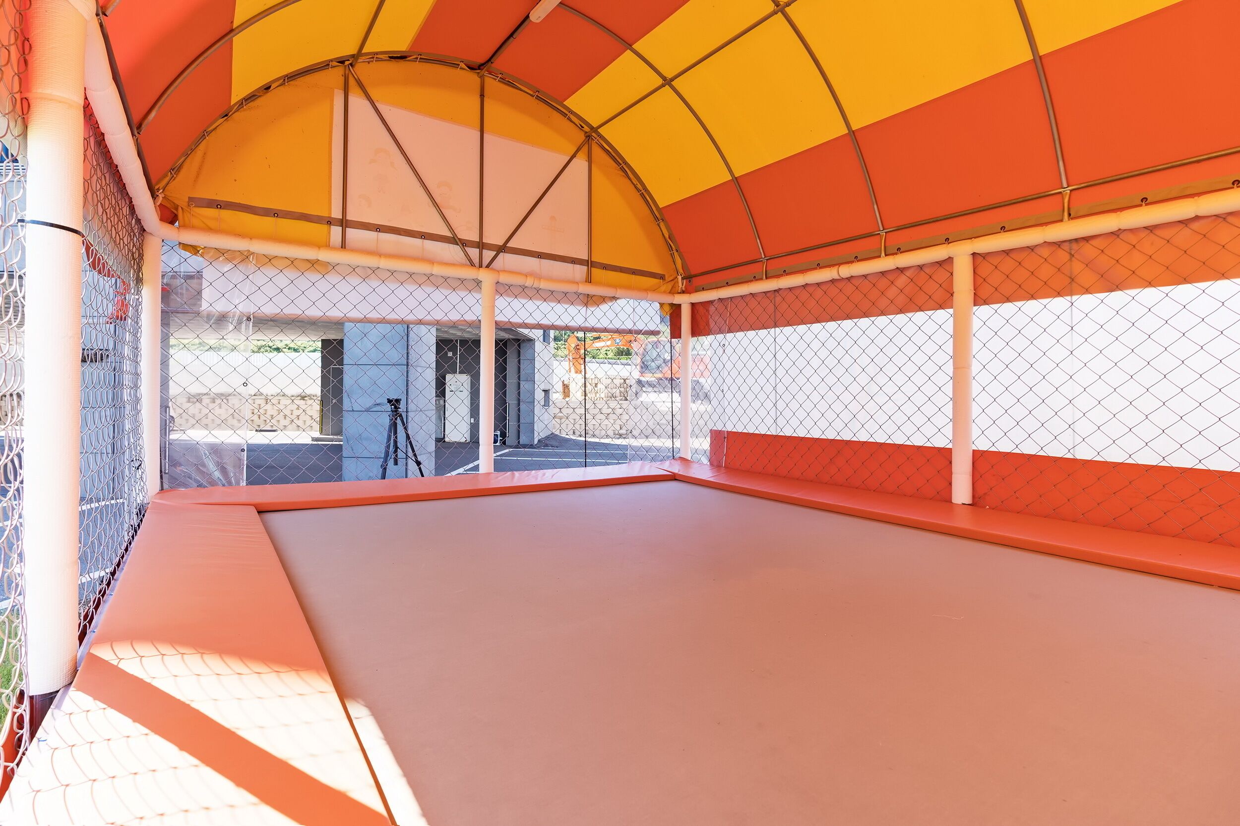 Zona de juegos interior con suelo acolchado, paredes de malla y un toldo colorido.