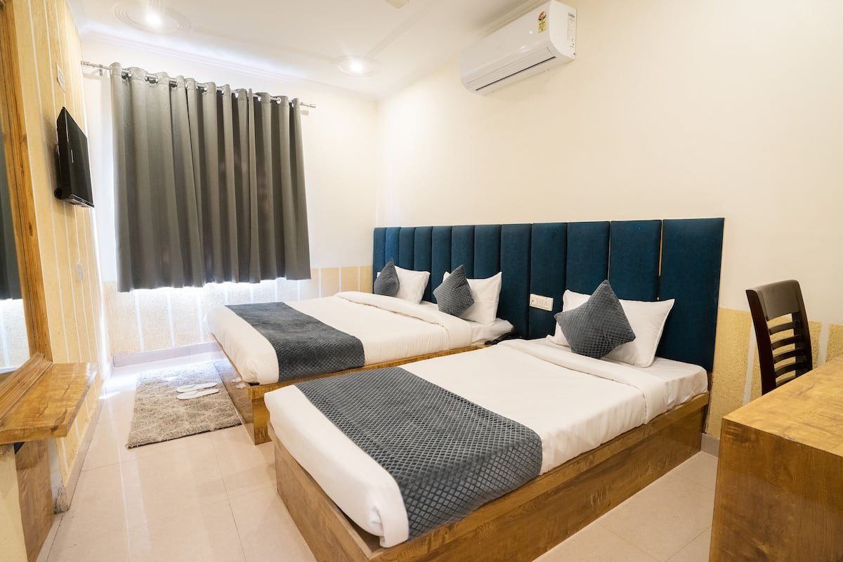 A hotel room with two beds, a wooden desk, a chair, a TV, and an air conditioning unit.