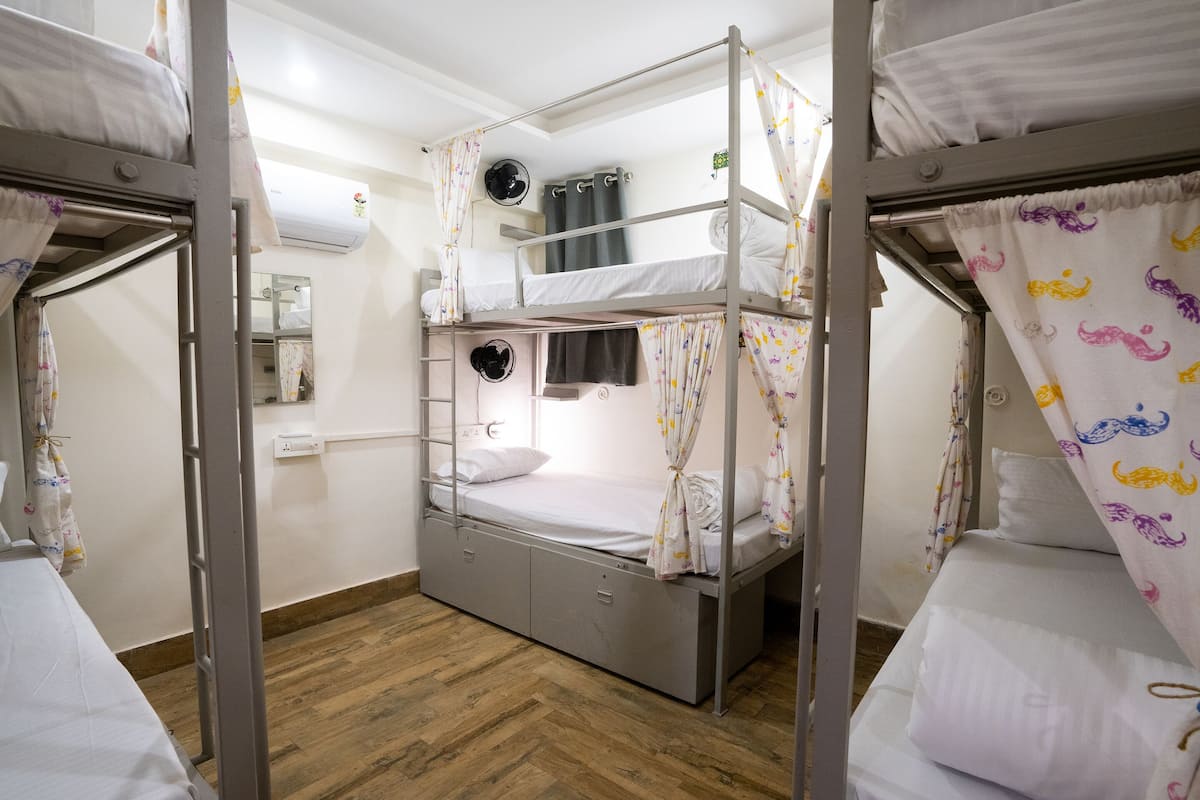A bunk bed room with a wooden floor, a mirror, and an air conditioning unit on the wall.