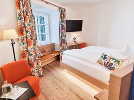 A hotel room with a bed, a desk, a chair, a TV, and a window with curtains.