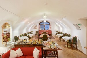 A dining area with multiple tables and chairs, a chandelier, and a red sofa.