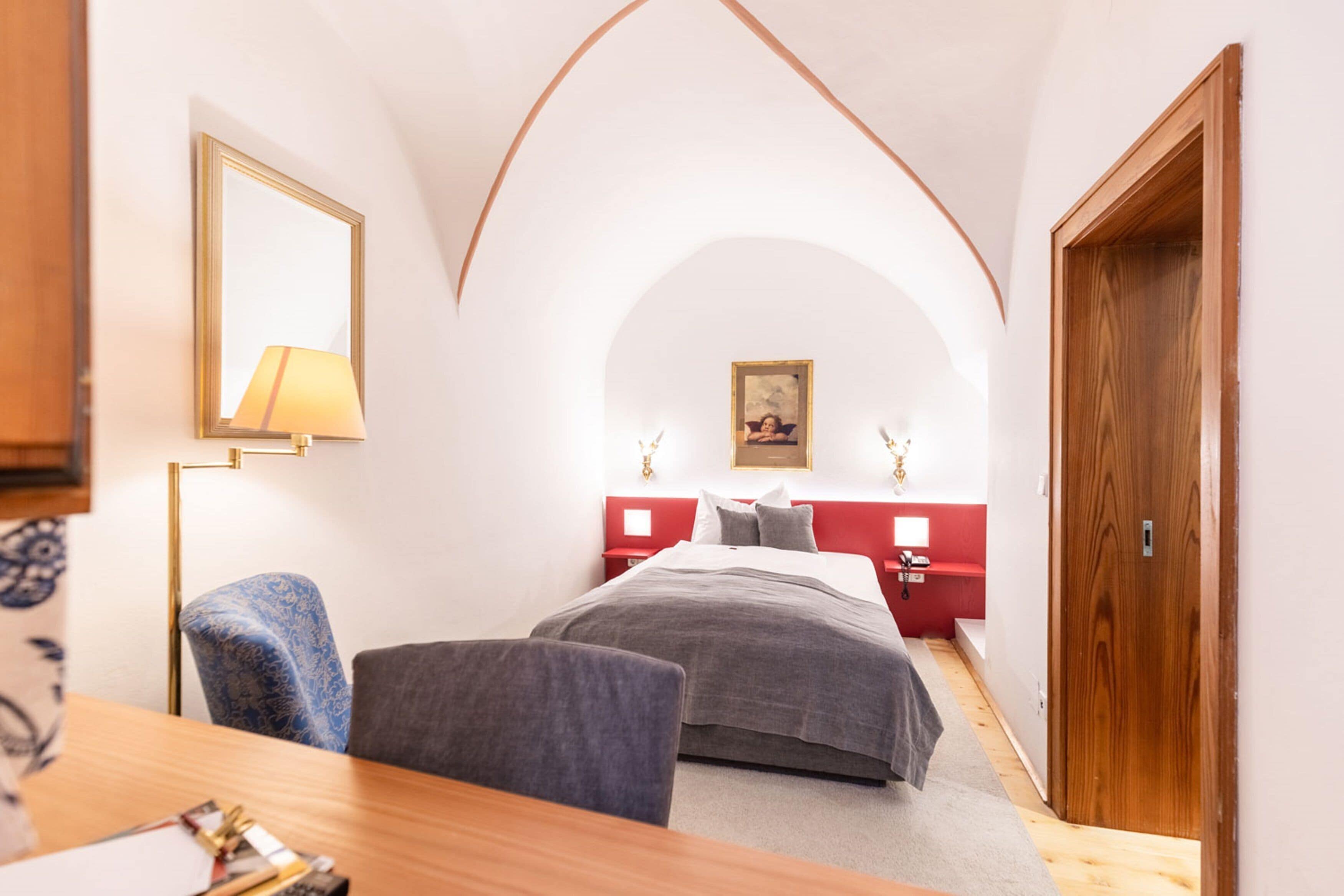Una camera da letto con un letto, una scrivania, una sedia, una lampada e una porta in legno.