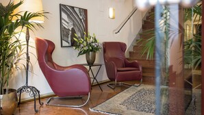 A modern interior with two red leather chairs, a floor lamp, a vase with flowers, and a staircase. - Altstadt Hotel Wolf (Salzburg)