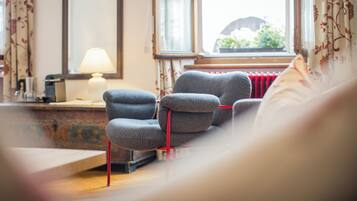 Un salón acogedor con un sillón gris, un radiador rojo y una ventana con vistas al exterior.
