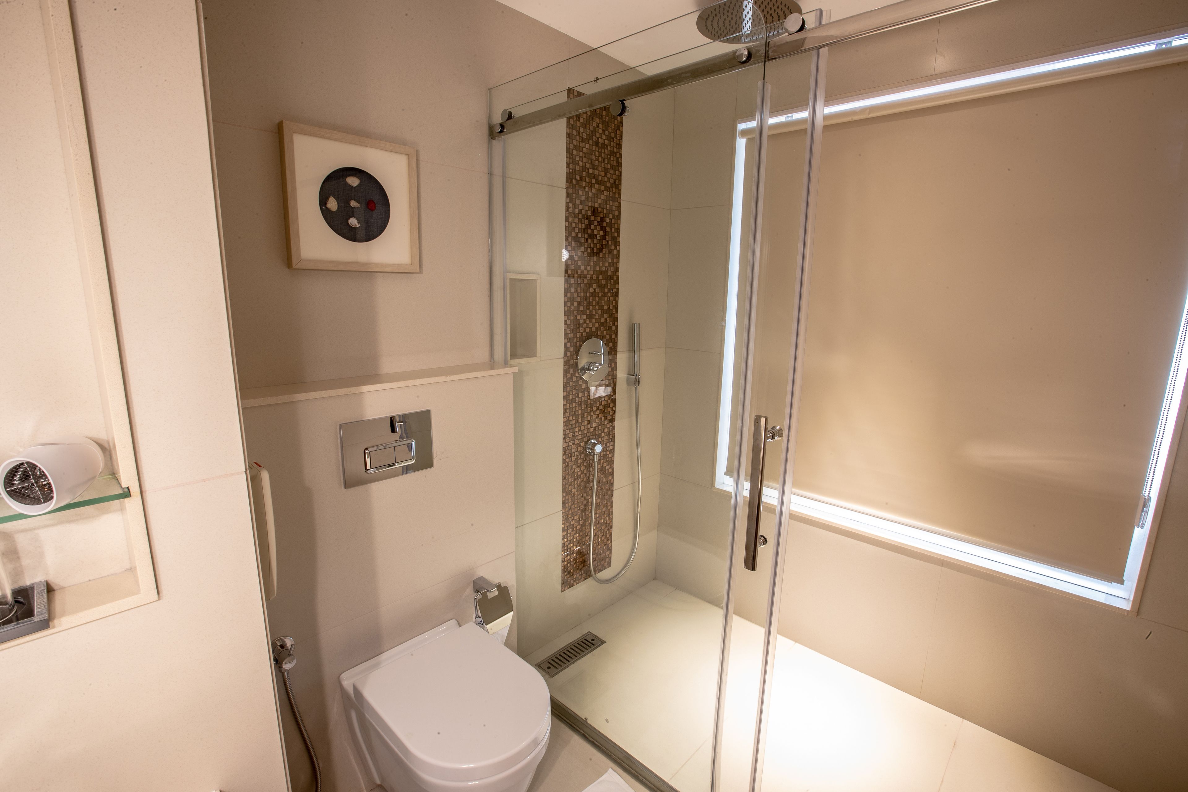 Een moderne badkamer met een douchecabine, toilet en een plankje met een haardroger.