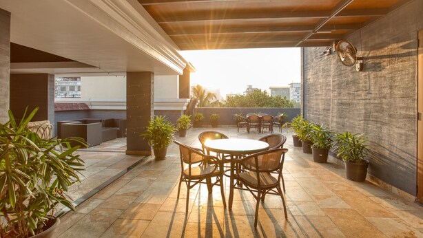 An outdoor patio area with a round table and chairs, surrounded by potted plants, under a wooden pergola. - Hotel Span International (Kanayannur)