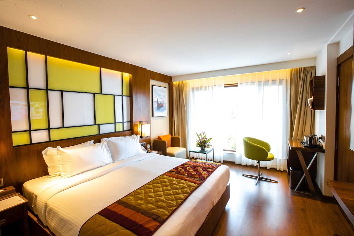 A hotel room with a large bed, a desk, a chair, and a window with curtains.