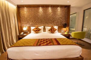 Una habitación de hotel con una cama grande, un cabecero de madera, una mesita de noche con un teléfono, una lámpara y una silla amarilla brillante.